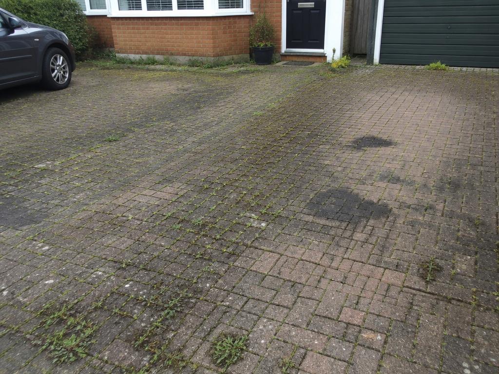 Block paved driveway covered in weeds, moss and oil stains before cleaning